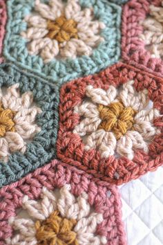 a crocheted blanket is laying on top of a bed with white and pink squares