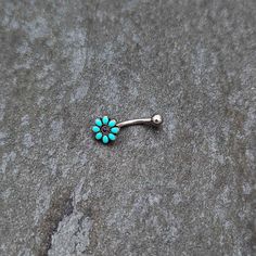 a pair of turquoise and silver colored flower shaped nose piercing studs on top of a rock