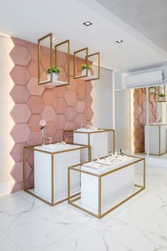 two white tables with gold frames in front of a pink hexagonal wall and planters