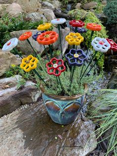 there are many different colored flowers in the pot on the rocks near some water and grass