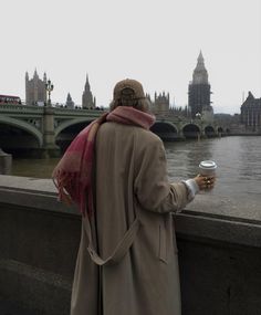 a man standing on the side of a bridge holding a cup of coffee