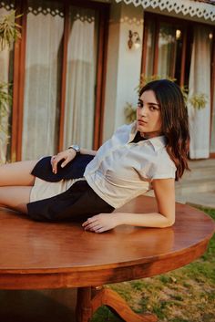 a woman sitting on top of a wooden table in front of a building with windows