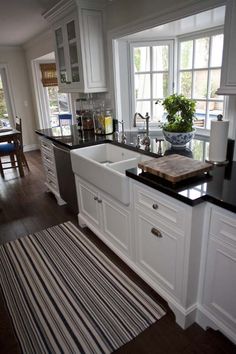 a kitchen with white cabinets and black counter tops, along with a striped rug on the floor