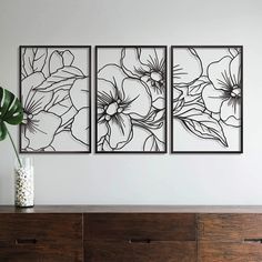 three black and white floral paintings on a wall above a dresser with a vase filled with flowers