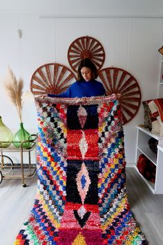 a woman sitting on top of a multicolored rug in front of a fan