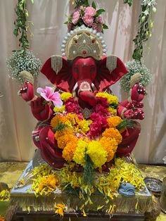 a statue of an elephant with flowers on it's head and two hands in the air