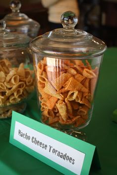 two glass jars filled with cheesy tortillas on top of a green table