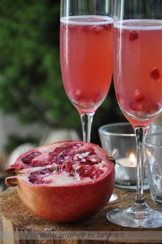 two glasses of pink wine and a pomegranate on a table with silver cups