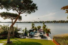 an outdoor deck overlooking the water with lounge chairs and trees in the foreground, on a sunny day