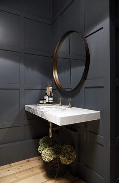 a white sink sitting under a mirror next to a wooden table with flowers on it