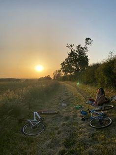 two people sitting on the side of a dirt road next to their bikes at sunset