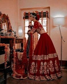 a woman in a red lehenga standing next to a table with flowers on it