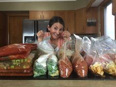 a woman standing in front of a counter filled with bags of food and vegetables, smiling at the camera