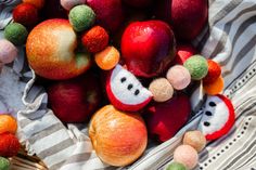 apples, oranges and other fruit are on a cloth bag with pom - poms