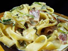 a plate full of pasta with bacon and asparagus on it, sitting on a wooden table