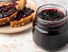 peanut butter and jelly sandwich on a plate next to a jar of jelly jam with two slices of bread in the background