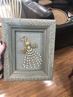 a person holding up a framed picture with bead work on it's side