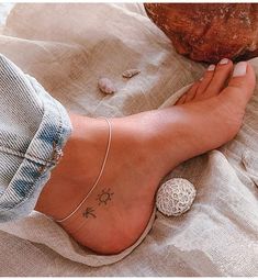 a woman's foot with a small star tattoo on her left ankle and two seashells in the background