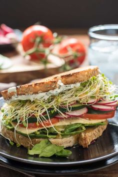 a sandwich with lettuce, tomatoes and other vegetables on a plate next to a glass of water