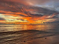 the sun is setting over the ocean with clouds in the sky and sand on the beach