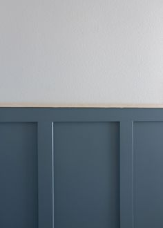 a white clock on top of a wooden shelf in front of a gray painted wall