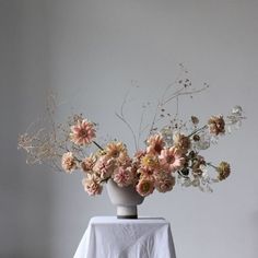 an arrangement of flowers in a white vase on a table with a white cloth draped over it