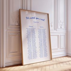 a wedding seating chart in front of a white paneled wall with wood flooring