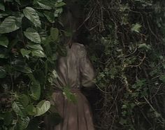 a woman standing in front of a bush with vines on it's sides and her back to the camera