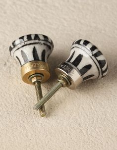 two black and white ceramic knobs with gold accents on each side, one has a screw in the middle