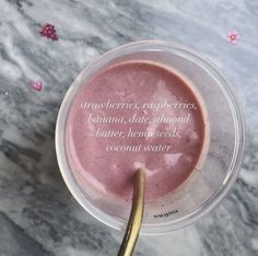 a pink smoothie in a plastic cup with a gold spoon