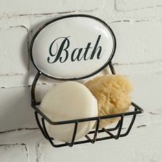 a soap bar and sponge in a metal basket on a white brick wall with the word bath above it