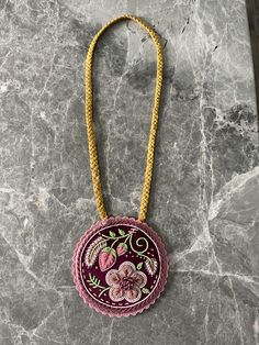 a necklace with flowers on it sitting on a marble surface next to a yellow cord