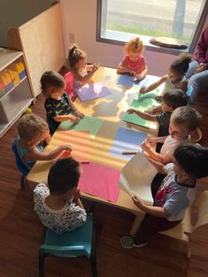 a group of children sitting at a table with paper on it and one child standing in front of the table