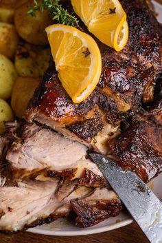 a plate with meat, potatoes and lemons on it next to a knife that has been cut in half