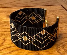 a black and gold woven bracelet on a wooden surface with two metal pins sticking out of it