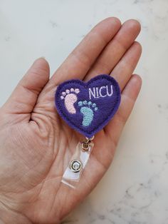 a hand holding a purple heart shaped badge with two footprints on it and the words nicu written in white