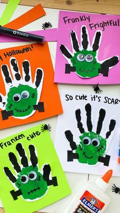 four handprinted halloween cards on a table with markers and glue, one is green and the other is orange