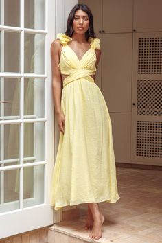 a woman in a yellow dress leaning against a wall