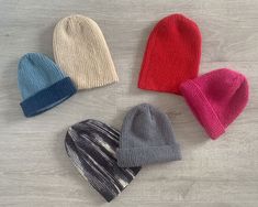 four knit beanies laid out on a wooden floor, all in different colors and sizes