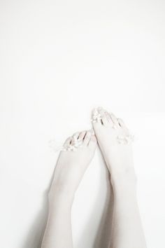 the legs of a woman with white nails and flowers on her toes, against a white background