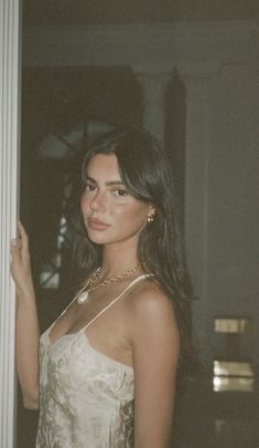 a woman standing next to a white wall wearing a dress and pearls on her necklace