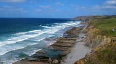 an aerial view of the ocean with waves coming in to shore and cliffs on either side