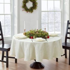 the table is set for christmas dinner with candles and greenery on it, along with two chairs