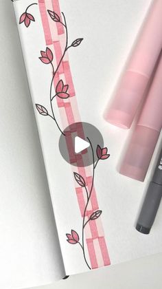 an open notebook with pink and white flowers on it next to two markers, one marker and the other pen