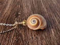 a necklace with a shell on it sitting on top of a wooden table next to a chain