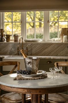 a kitchen table with two chairs and a wine glass on it in front of a window