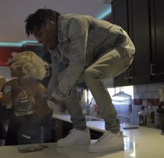 a man standing on top of a kitchen counter next to a blonde haired woman in white shoes