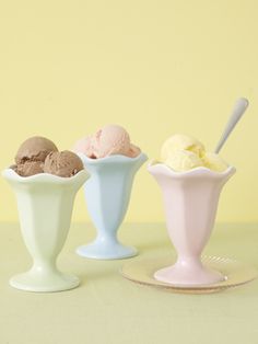 three ice creams in small white bowls on a yellow surface with a spoon next to them