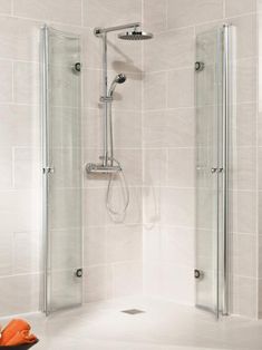 a walk in shower sitting next to a white tiled wall and floor with an orange object on the ground