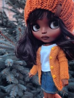 a close up of a doll wearing a knitted hat and jacket with long dark hair